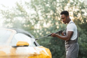 Washing outside rearview car mirror with high pressure water at self car wash service outdoors.